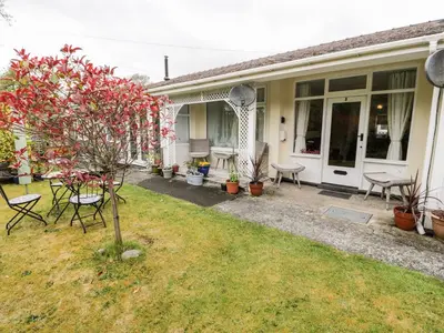 a house with a yard with chairs and a tree at 3 Riverside Bungalows in Llanbedr