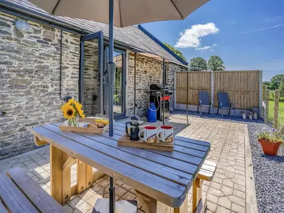 a wooden picnic table with an umbrella on a patio at The Old Cowsheds 4 - Daniel Ddu - Uk49789 in Cribyn