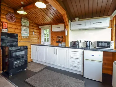 a kitchen with white cabinets and a black stove at Y Bwthyn Pren, Cabin 209, in Trawsfynydd