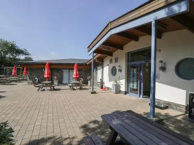 a patio with picnic tables and red umbrellas next to a building at 8 Puffin Way in Llwyngwril