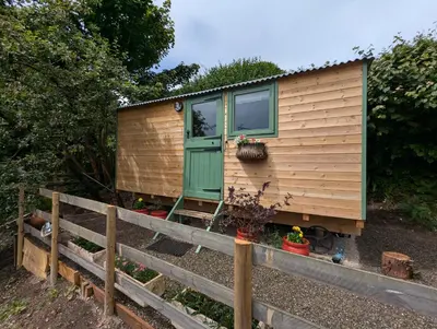 a tiny house with a green door and a fence at Myndy The Shepherd's Hut in Church Stretton