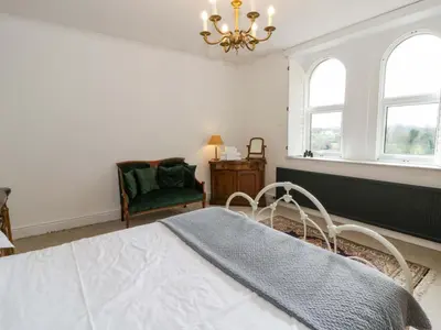 a bedroom with a bed and a chair and windows at The Retreat at Glanrannell Park House in Llanwrda