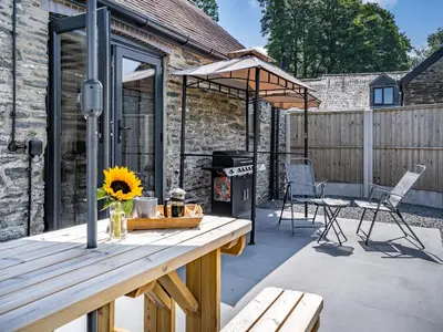 a patio with a table with a grill and chairs at The Old Cowsheds 1- Dairy - Uk49786 in Cribyn