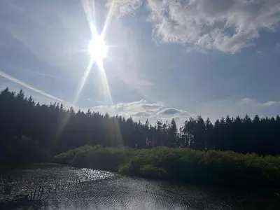 a sun is shining over a river with trees at Bell Tent - Lakeside in Oswestry