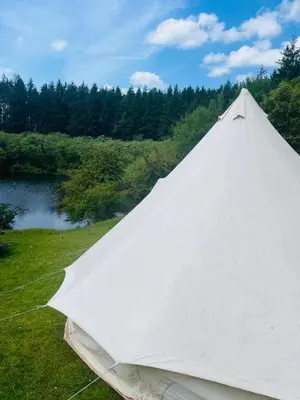 a large white tent in the grass next to a lake at Bell Tent - Lakeside in Oswestry