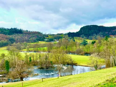 a river in the middle of a grassy field next to a river at Outstanding Llangollen Riverside Apartment in Llangollen