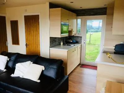 a living room with a black couch and a kitchen at Snowdonia 1-Bed Chalet Sleeps 2 Stunning Views in Pennal