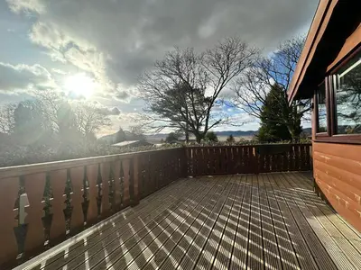 a deck with a fence and the sun in the sky at Caban Enfys in Trawsfynydd