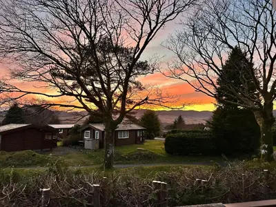 a house with a tree and a sunset in the background at Caban Enfys in Trawsfynydd