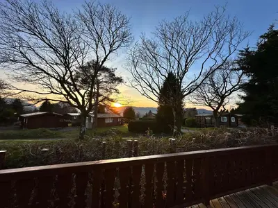 a sunset over a yard with trees and a bench at Caban Enfys in Trawsfynydd