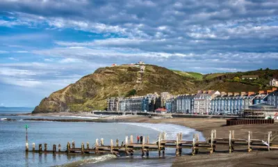 a beach with a pier and buildings and a hill at Ty Sunnymead Guesthouse in Aberystwyth