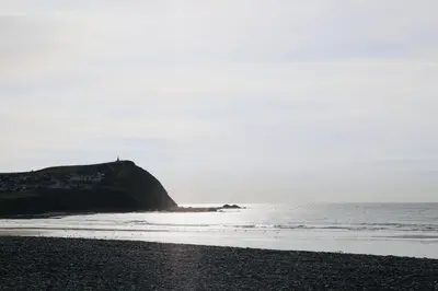 a beach with a rock in the ocean with a lighthouse at Woodcutters' Cabin Authentic Log Cabin Talybont Aberystwyth SY245DW in Aberystwyth