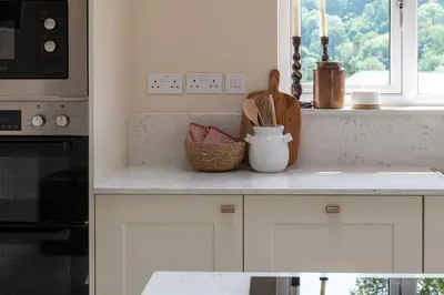 a kitchen with white cabinets and a counter with a window at Swn y Nant in Glyn-Ceiriog