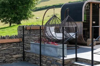 a patio with a swing and a rock wall at Swn y Nant in Glyn-Ceiriog