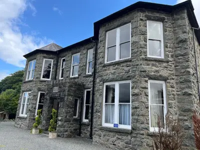an old stone house with white windows on a sunny day at Bala Suite at pen Y Coed Hall in Dolgellau