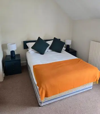 a bedroom with a bed with an orange blanket on it at Community Owned Gwesty Owain Glyndwr Hotel in Corwen