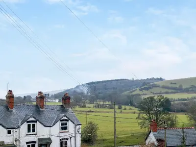 a white house in a field with hills in the background at Swan Cottage in Carrog