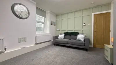 a living room with a couch and a clock on the wall at Barmouth Beach Ground Floor Studio in Barmouth