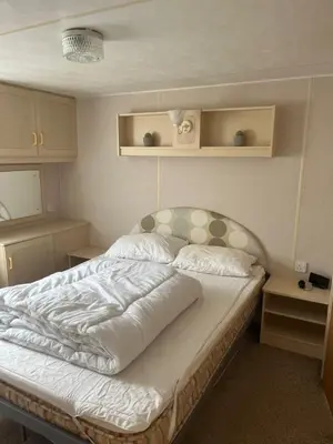 a bedroom with a bed with white sheets and pillows at Static Caravan in Aberystwyth