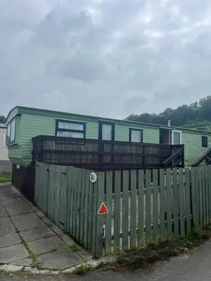 a green house behind a wooden fence with a house at Static Caravan in Aberystwyth