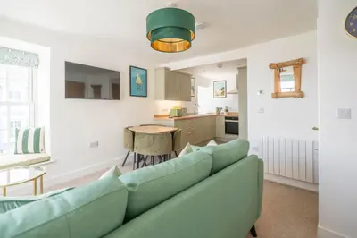 a living room with a green couch and a kitchen at Mermaid's Apartment by Ty Annie Holidays in New Quay