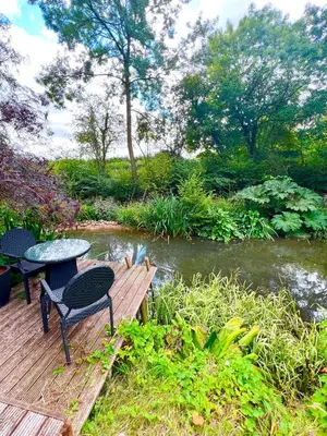 a table and chairs on a wooden deck next to a river at Storeybook cottage in Oswestry