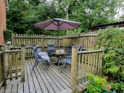 a wooden deck with a table and an umbrella at 2 Aqueduct Cottages in Wrexham