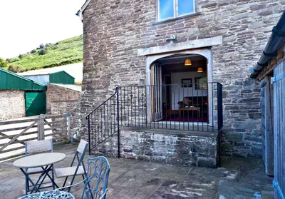 a patio with chairs and a table and a building at Mountain View Farm Cottage in Crickhowell