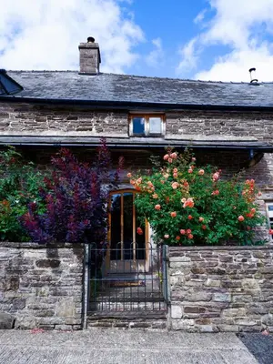 an old stone house with a gate and flowers at Mountain View Farm Cottage in Crickhowell