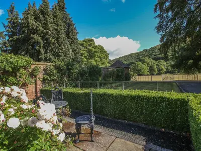 a garden with a table and chairs and a hedge at Courtyard Cottage in Church Stretton