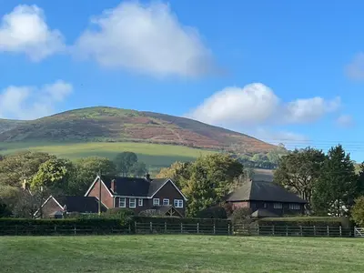 a house in a field with a hill in the background at Courtyard Cottage in Church Stretton