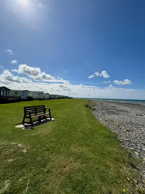 a bench sitting on the grass near the beach at T&J Seaview at Pengarreg in Llanrhystyd
