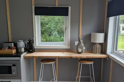 a kitchen with a counter with stools and a window at Tranquil Cabin Retreat- Sleeps 2 Parking in Welshpool