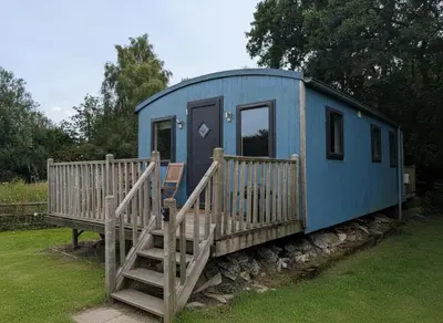 a blue tiny house with a wooden porch and stairs at Tranquil Cabin Retreat- Sleeps 2 Parking in Welshpool