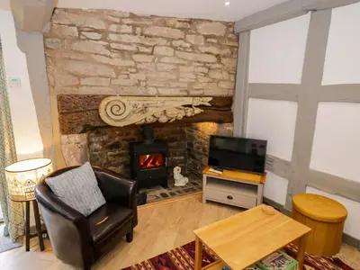 a living room with a fireplace and a chair and a television at Middle Cottage in Ludlow
