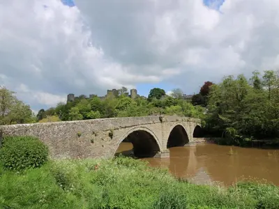 a stone bridge over a river with a castle in the background at Middle Cottage in Ludlow
