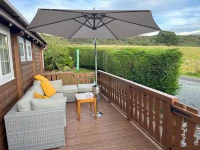 a patio with a couch and an umbrella on a deck at Log Cabin Retreat Snowdonia in Trawsfynydd