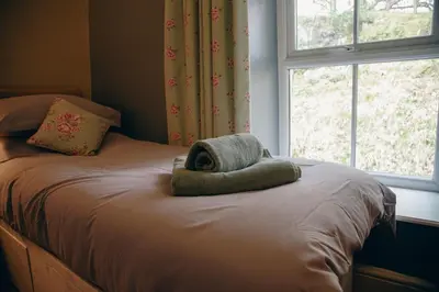 a bed with a towel on it with a window at Little Cott - Cosy Welsh Cottage, a hiking retreat in Maentwrog
