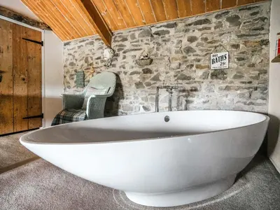 a white bath tub in a room with a stone wall at Ty Fferm Bargoed in Aberaeron