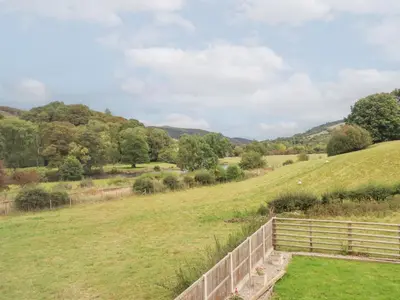 a field with a fence and mountains in the background at Plas Yn Bonwm in Corwen