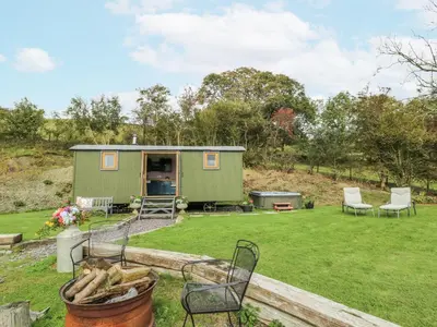 a green tiny house in a yard with chairs at Brondel Luxury Shepherd's Hut in Aberystwyth