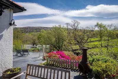 a wooden bench sitting next to a garden with flowers at Artro in Llanbedr