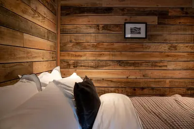 a bedroom with wooden walls and a bed with white pillows at Woolly Wood Cabins - Nant in Abbey-Cwmhir