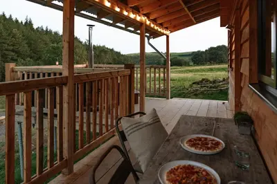 two pizzas sitting on a wooden table on a porch at Woolly Wood Cabins - Nant in Abbey-Cwmhir