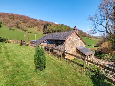 a stone barn in a field next to a fence at Lower Rheol in Erwood