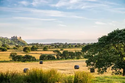 a field with hay bales in it with a castle in the background at Stabl-Bennar in Dyffryn
