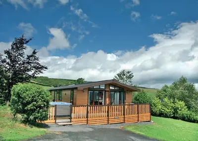 a small house with a wooden fence in a field at Belan Bach Lodges in Towyn