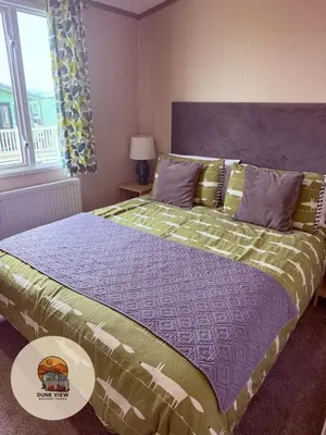 a bedroom with a bed with a purple and green comforter at Dune View Caravan in Ynys-lâs Station