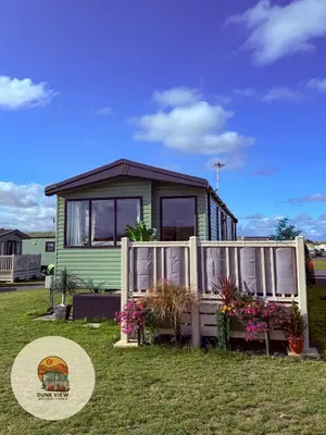 a green tiny house with a fence and flowers at Dune View Caravan in Ynys-lâs Station