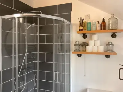 a shower in a bathroom with black tiles at Archers Cottage in Leominster